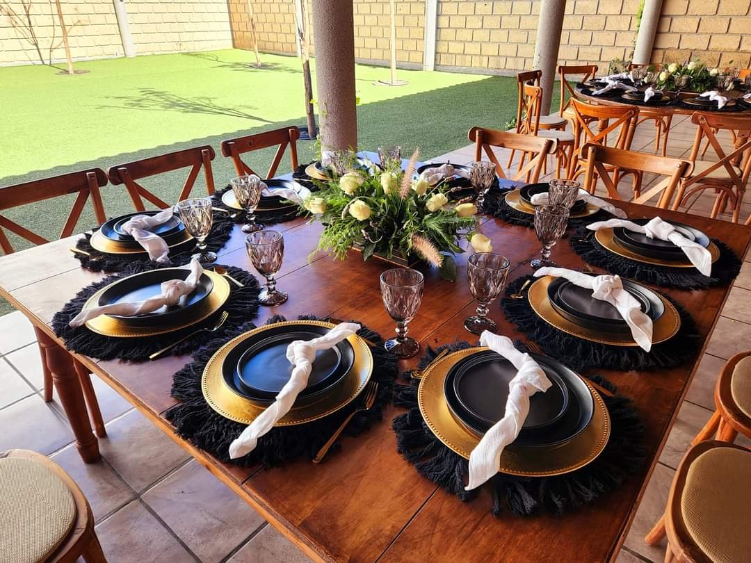 Mesa de evento decorada con vajilla negra, bases doradas, copas talladas y centro de mesa floral elegante.